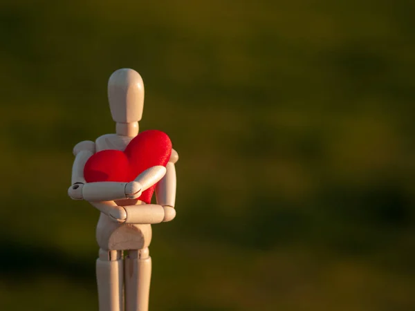 Деревянный манекен обнимает свое сердце руками Концепция романтизма и любви — стоковое фото