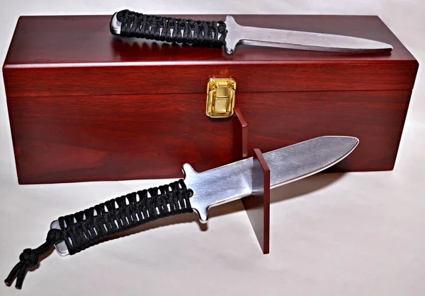 Two aluminum training knifes with rope handle at wooden box
