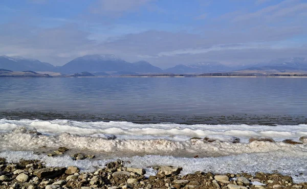 Bande de neige au bord du lac avec des montagnes en arrière-plan — Photo