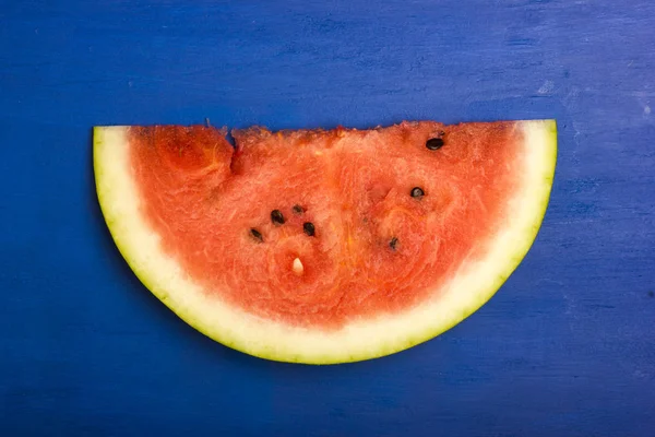 Um pedaço de uma melancia madura e doce sobre um fundo azul de madeira — Fotografia de Stock