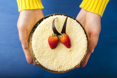 Beyaz çikolata ve taze çilek ile kek, kadınların elleri tutun. Mavi bir arka plan üzerinde lezzetli tatlı 