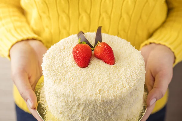 Beyaz çikolata ve taze çilek ile kek, kadınların elleri tutun. Mavi bir arka plan üzerinde lezzetli tatlı 