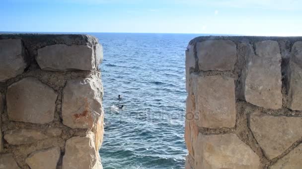 Mar y nadadores a través de una pared de piedra — Vídeo de stock