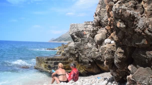 Mélange de 2 coups de feu, petite-fille et grand-mère assis sur le bord de la mer — Video