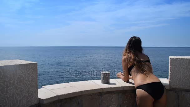 Молодая женщина в бикини выходит на балкон, чтобы насладиться красотой открытого моря — стоковое видео