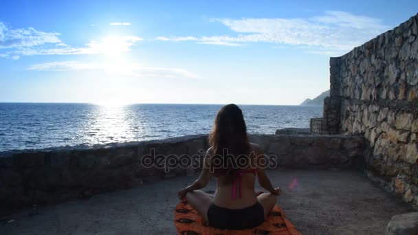 Meisje in badpak beginnen meditatie tegenover de zee en de zon — Stockvideo