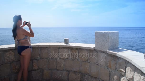 Ung brunett i bikini fotografera havet från balkongen — Stockvideo