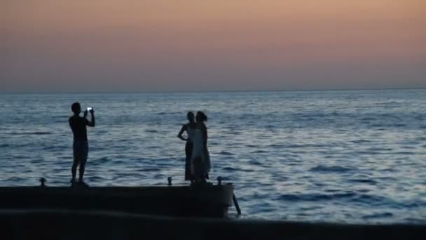 Muž fotografování dvě ženy na pláži při západu slunce — Stock video