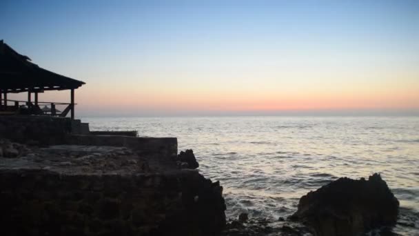 Zonsondergang op een rotsachtige strand met een vervallen huis van riet — Stockvideo