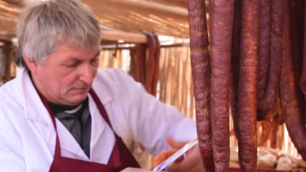 Ouderen grijs-haired mens bereidt zelfgemaakte varkensvlees worst op de grill, varken slachten festival, Belo Blato, Vojovina, Servië, 12 maart 2017. — Stockvideo