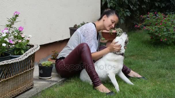 Chica abrazar a su perro sobre la cabeza mientras él sostiene una pelota de tenis en su boca — Vídeos de Stock