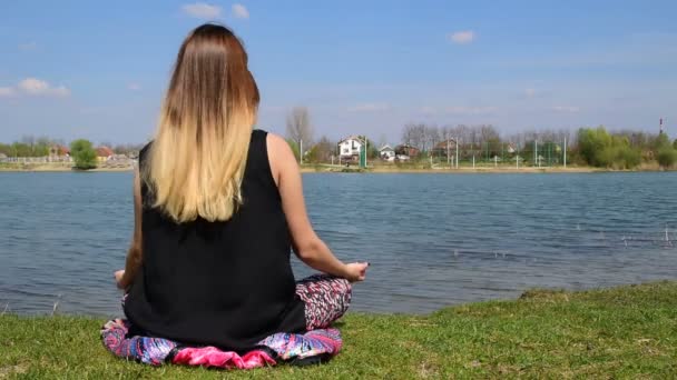 Niña meditando en la posición de loto cerca del agua — Vídeo de stock