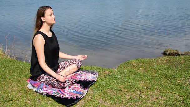 Joven hembra meditando junto al agua en posición de loto — Vídeo de stock