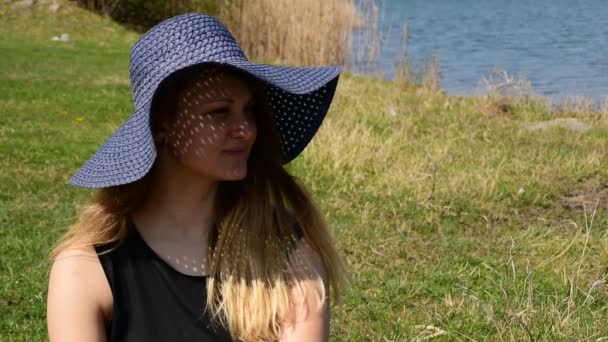 Молода дівчина з капелюхом насолоджується природою біля води — стокове відео