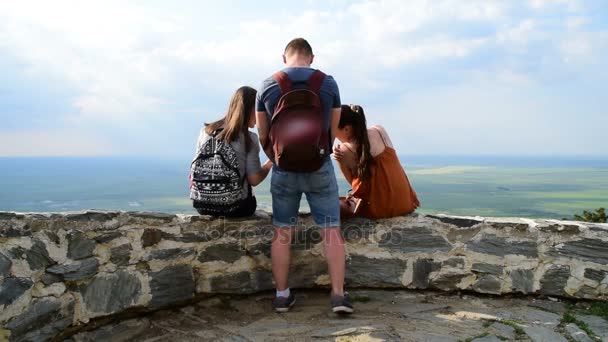 Üç arkadaş (bir erkek ve iki kadın) kale, yüksek bakış açısı ve vadi içinde belgili tanımlık geçmiş duvardaki dinlenme — Stok video