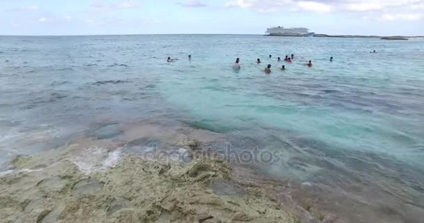Ondas salpicando uma rocha e turistas nadando na distância — Vídeo de Stock