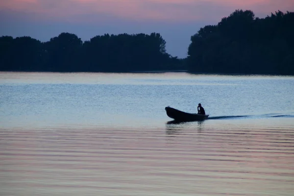 Silhouet van een man in een boot die in de rivier bij zonsondergang zweeft — Stockfoto