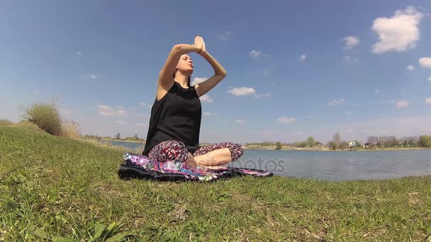 En tjej som gör yoga praxis i naturen nära sjön — Stockvideo