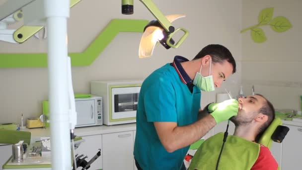 Молодой человек в кабинете дантиста, запечатывает зуб — стоковое видео