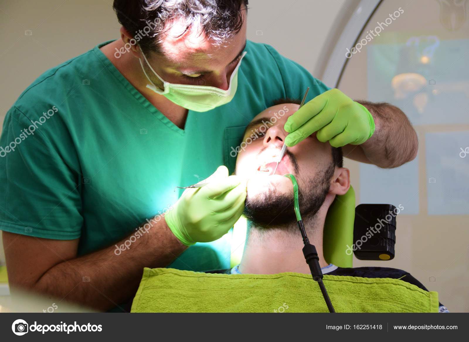 Young handsome man sitting on dental chair while his young male dentist