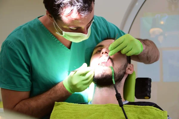 Genç erkek dişçisi onun teeths giderir iken diş sandalyede oturan genç yakışıklı adam