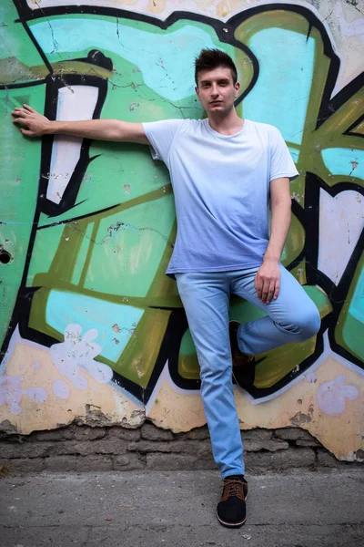 Jovem posando ao lado de uma parede rústica pintada com grafite — Fotografia de Stock