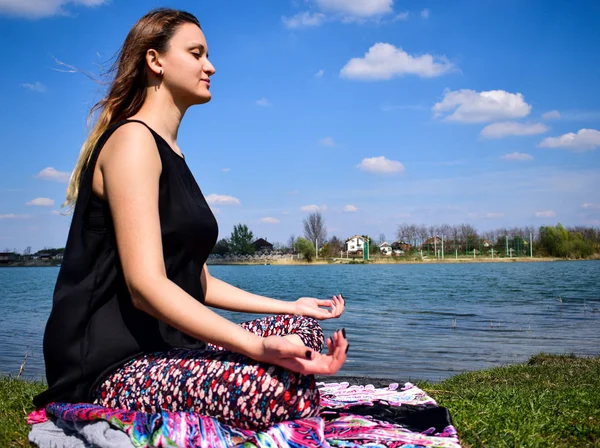 Mujeres jóvenes meditando junto al agua en posición de loto — Foto de Stock