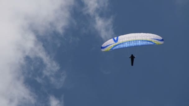 Adam mavi gökyüzü üzerinde yamaç paraşütü yönetir — Stok video