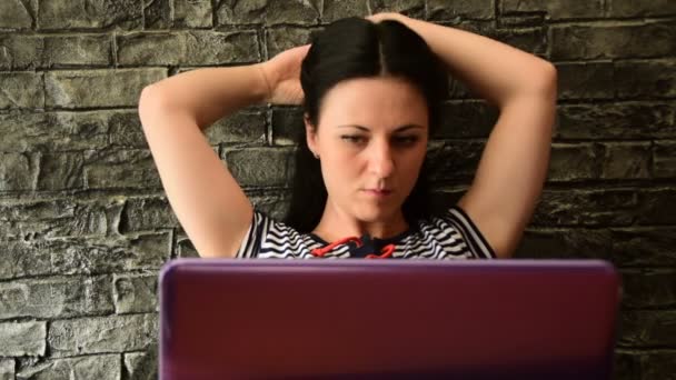 Een jonge vrouw bevestigt haar haar en zet haar werkzaamheden voort op de laptop — Stockvideo