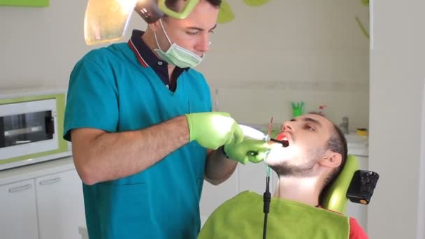 2 в 1, запечатування зуба розпадом, молодий чоловік в стоматологічному кабінеті — стокове відео
