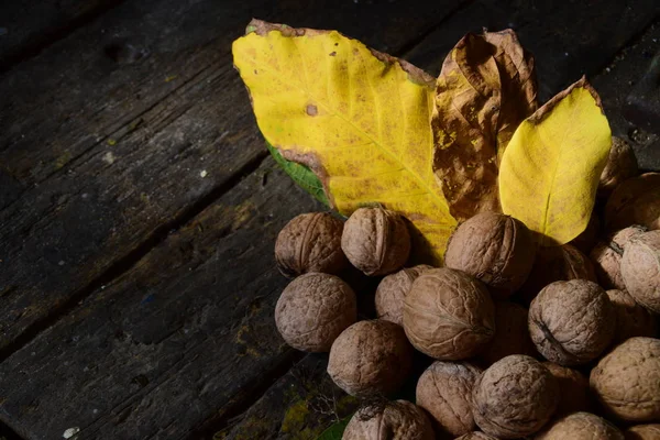 Yellow leaves and a bunch of walnuts on a wooden table — Stock Photo, Image