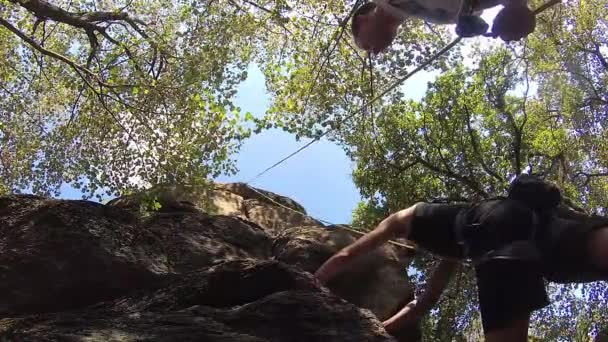 4k, een jongere man klimt tot de rock, rock klimmen apparatuur, team vrije klimmen, schot uit de onderstaande lijst — Stockvideo