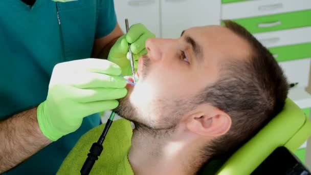 Close-ups, mãos dentárias em luvas verdes, fixação de dentes de um paciente do sexo masculino — Vídeo de Stock