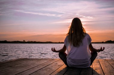 Göl kenarındaki ahşap duba üzerinde meditasyon yoga konumda genç kadın 