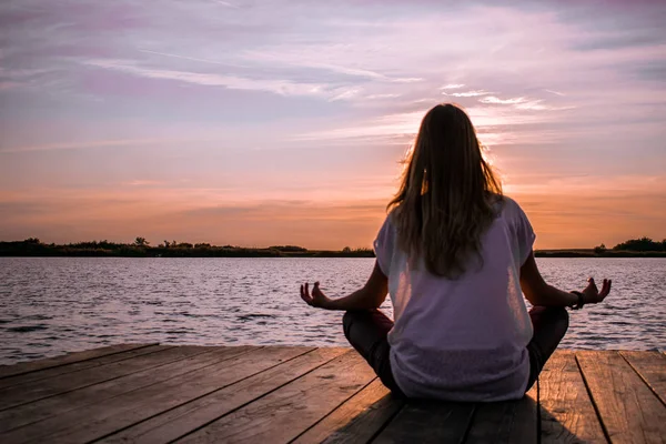 Unga kvinnor i meditativ yoga position på trä ponton på sjön — Stockfoto