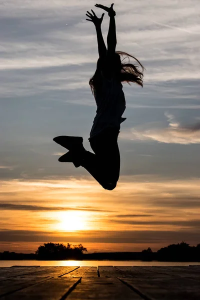 Silueta de mujer saltando sobre el lago frente a la puesta de sol — Foto de Stock