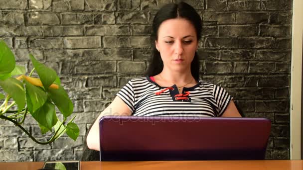 Casual jonge vrouw met een laptop in haar bureau, werkt, luistert naar muziek, ze houdt van haar werk, het rode hart rechtsboven wordt weergegeven — Stockvideo