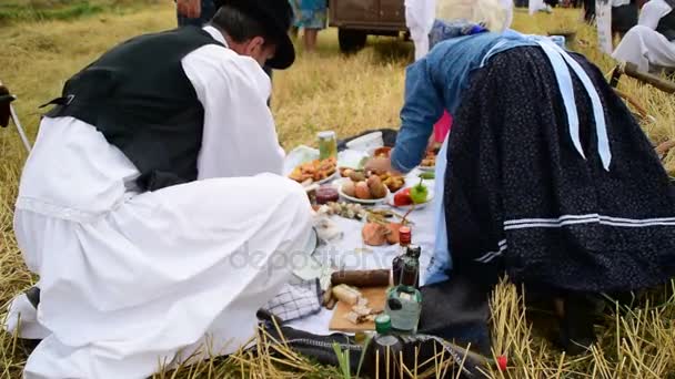Hombres y mujeres en trajes nacionales preparando un almuerzo para los trabajadores en el campo, un desayuno al aire libre en el campo — Vídeo de stock