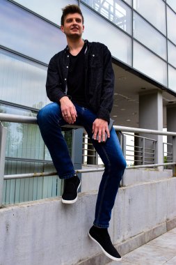 bir korkuluk cam bina karşı üzerinde oturan rahat genç adam