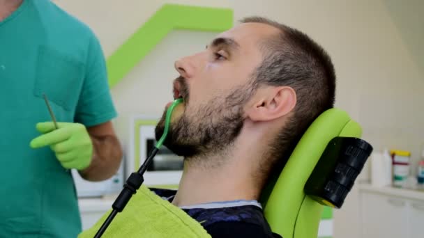 Joven hombre guapo sentado en la silla dental mientras su dentista arregla sus dientes, la limpieza de los dientes de la caries — Vídeo de stock