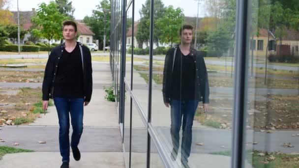 ガラスの建物に立っている、スマート フォンを使ってカジュアルな都市の若い男 — ストック動画