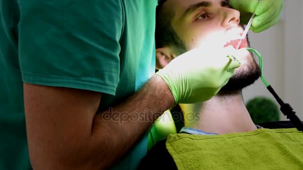 Крупним планом, зубні руки в зелених рукавичках, фіксуючи зуби пацієнта чоловічої статі — стокове відео