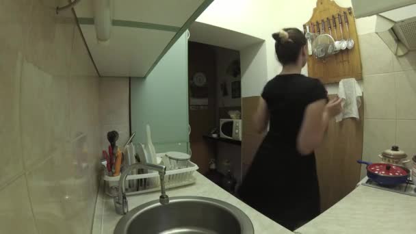 4k, una chica en un vestido negro bailando en la cocina, comprobando el almuerzo, atrapando plátano y disparando en la cámara — Vídeos de Stock