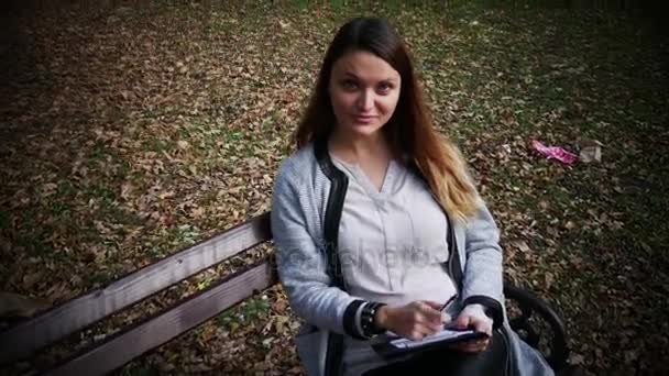 Gyönyörű fiatal nő az írás egy napló kint a parkban, a hallgató tanul egy padon a parkban, diák lány felkészülés a vizsgára, a természet — Stock videók