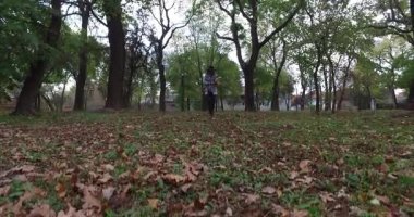 Park başında siyah bir şapka ile genç bir kadın taşıyan kitapları, kağıtları, belgeler, çalışma kamera yürür