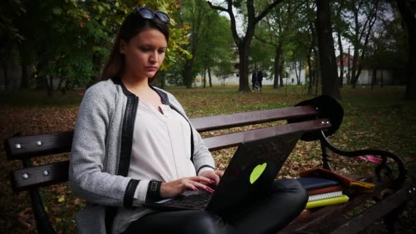 Молодая женщина, работающая на ноутбуке в офисе на открытом воздухе, паркуется осенью — стоковое видео