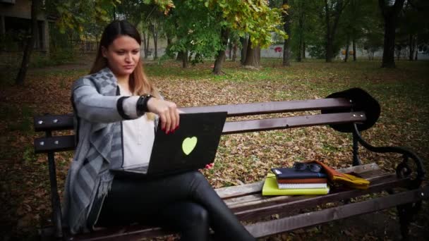 一个年轻的妇女从长凳上拿起笔记本电脑, 开始在它的工作, 户外办公室, 公园在秋季 — 图库视频影像