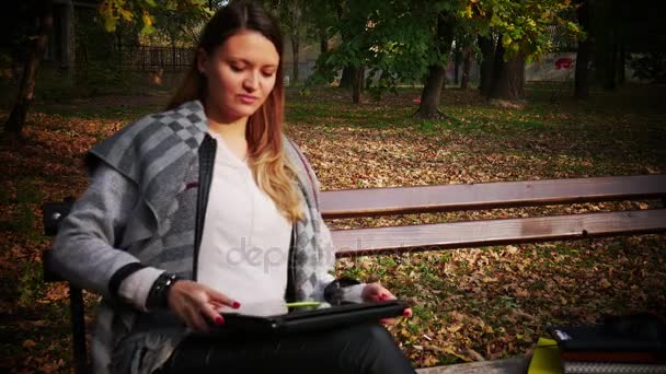 Молодая женщина берет ноутбук со скамейки и начинает работать над ним, открытый офис, парк осенью — стоковое видео