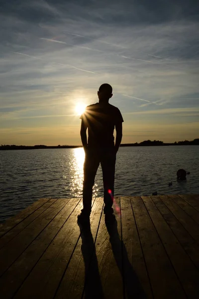 Silhouette eines jungen Mannes am See vor dem Sonnenuntergang — Stockfoto