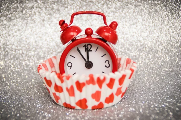 a small red clock in a paper basket for cookies with hearts, shows 5 minutes to midnight, a happy new year, five minutes to twelve, white snow background,  It\'s time to make a baby, it\'s time for safe sex